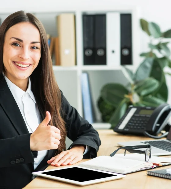 empresaria-joven-sonriente-que-sienta-lugar-trabajo-que-muestra-pulgar-encima-muestra_23-2147943730